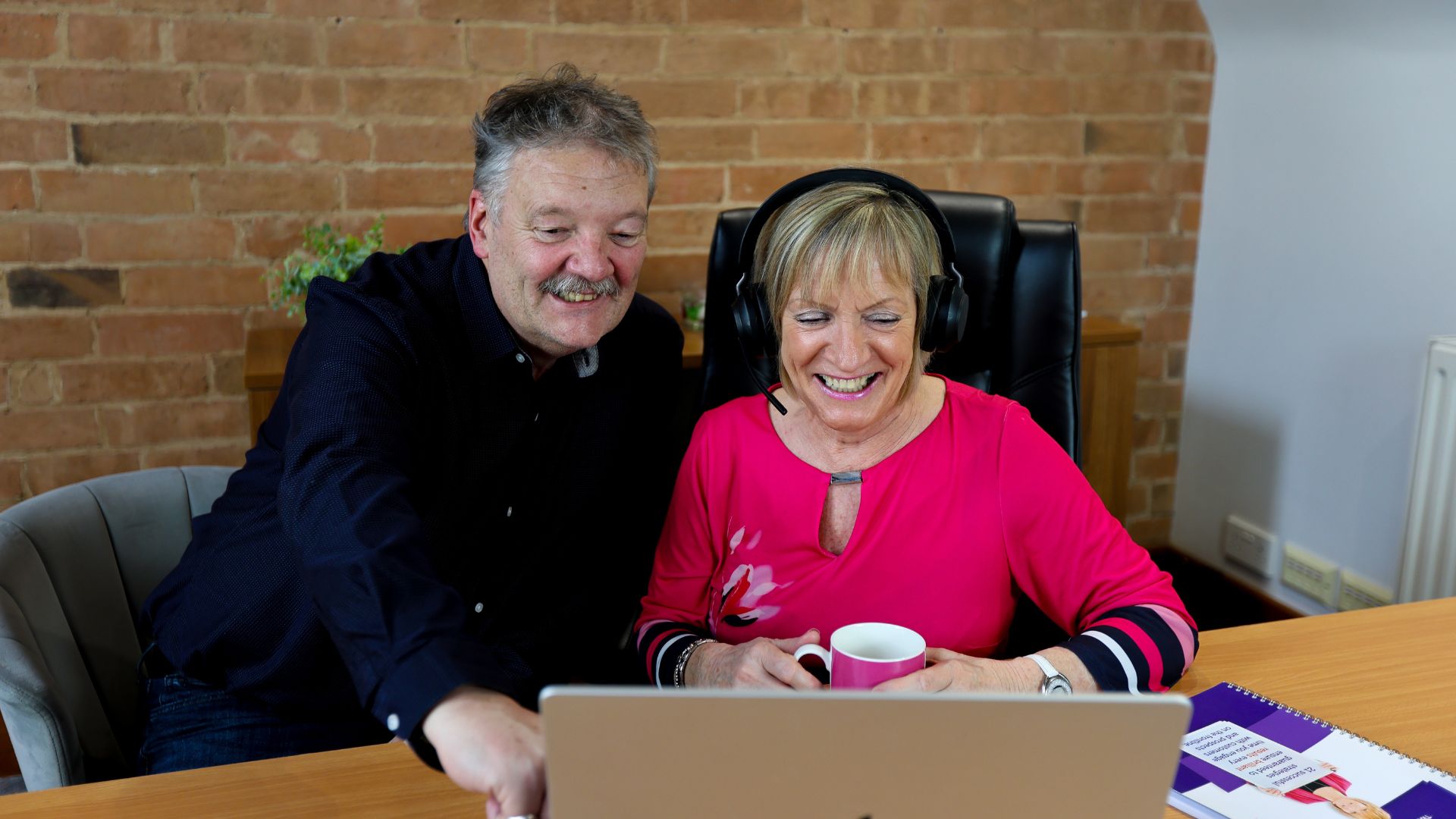 David-Marie David and Marie Cross sitting at a desk, smiling and looking at a laptop screen.