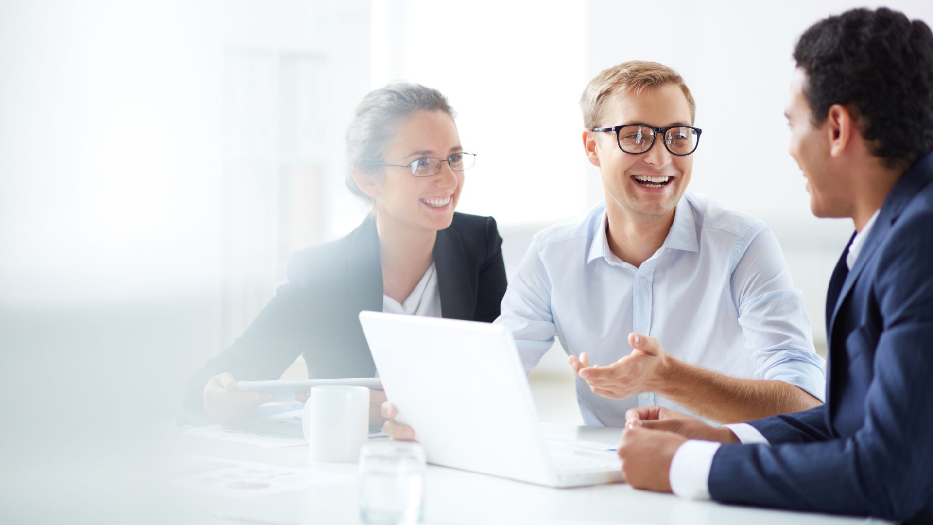 People A group of three professionals in smart clothing smiling and discussing ideas around a laptop.