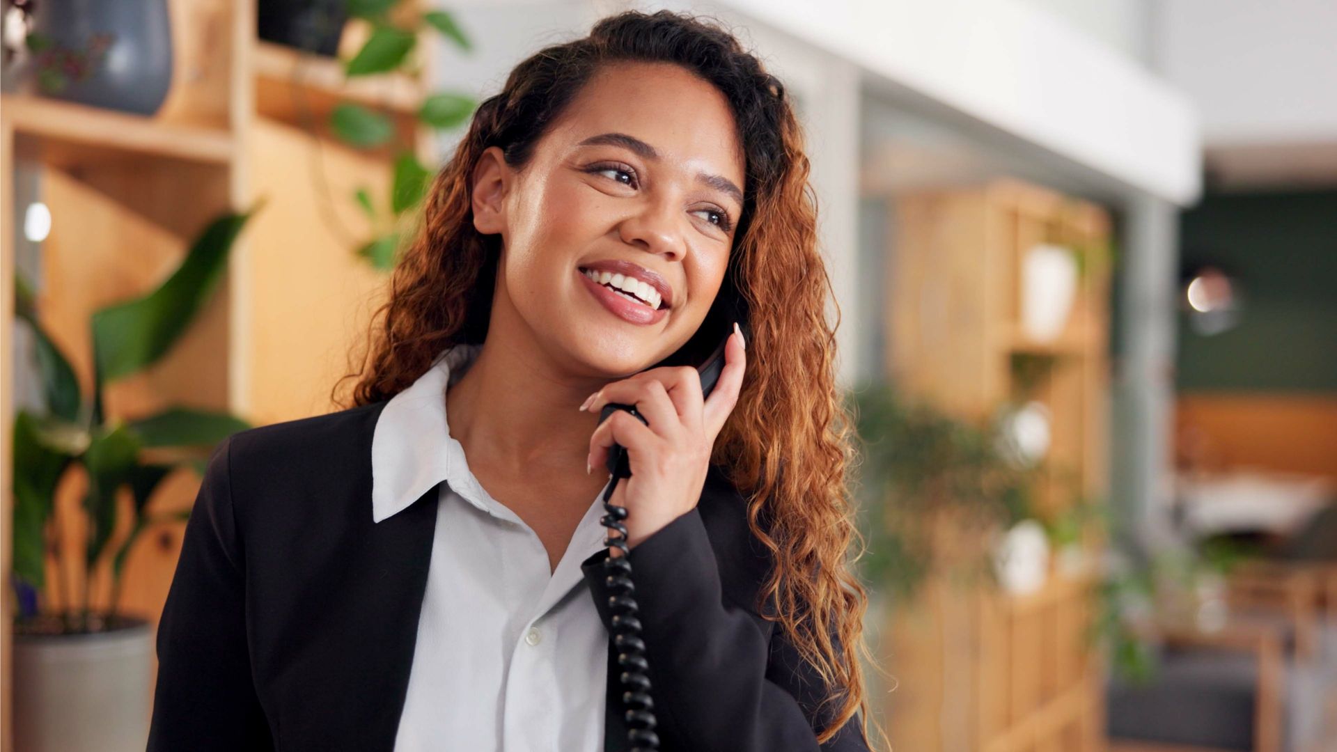 A young professional in a light shirt and dark blazer smiling and talking on the phone. 